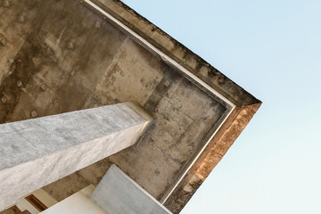A low-angle shot of a concrete building, emphasizing the architectural details of the overhang and the supporting pillar
