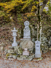 A standing stone statue of a Bodhisattva, set against a rocky forest backdrop, with accompanying...