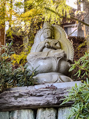 Obraz premium A serene stone Buddha statue, set against a forested background with sunlight filtering through autumn leaves, creates a tranquil and spiritual scene amidst nature.
