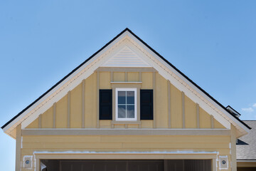 Under construction yellow garage gable roof with decorative window with dark shades, white gable vent 