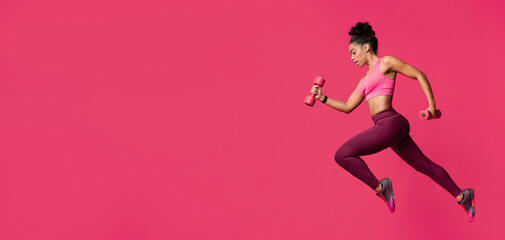 Active young black woman training wth dumbbells over red background, side view
