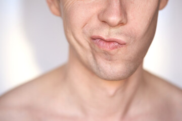 Close-up of uncertain expression on man face with pursed lips against neutral background