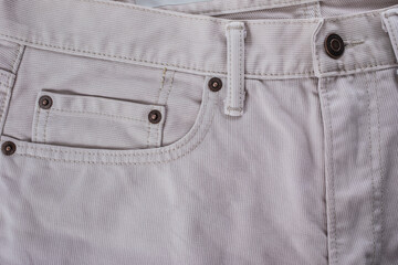 Close-up of a beige denim jeans pocket with a leather jacket detail on white background