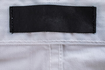 Close-up of a blank brown leather label on a denim jeans pocket, showing the rough texture of the fabric and the contrast between the leather and denim