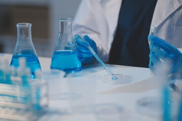 Group of dedicated scientist conduct chemical experiment in medical laboratory, carefully drop precise amount of liquid from pipette into test tube for vaccine drug or antibiotic development. Neoteric