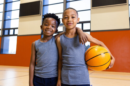 Fototapeta In school gym, two multiracial boys smiling and holding basketball, enjoying sports activities
