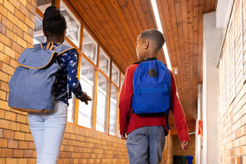 Walking in school hallway, two multiracial boy and girl with backpacks heading to classroom