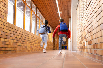 Running down school hallway, multiracial boy and girl with backpacks heading to classroom