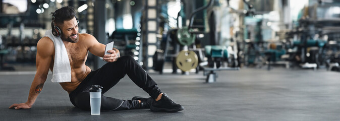 Online personal trainer on mobile phone. Muscular man using cellphone at gym, free space, web-banner