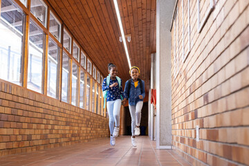 Running in school hallway, two african american girls with backpacks smiling and having fun