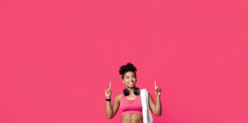 New ladies gym opening. Happy african american sporty girl with towel and earphones pointing up over red background
