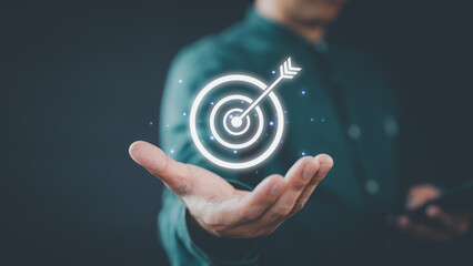 A businessman holds a glowing digital target with an arrow in the center, symbolizing focus and goal achievement. The futuristic design highlights innovation and success.