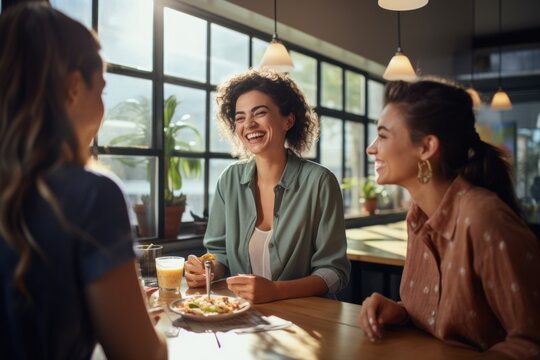 Three friends share a joyful moment, laughing together over brunch at a cozy, sunlit café with large windows and green plants.