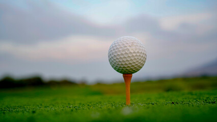 Golf ball on tee with sunrise background.