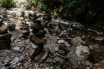 Stacked stones along a serene riverbank in a tranquil forest setting during a sunny afternoon
