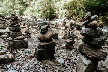 Stacked stones create a tranquil landscape in a forested area near a rocky riverbank at midday