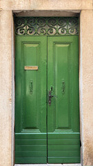 old wooden green door with ornate iron on top against stone frame