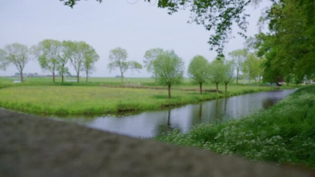 A close-up of a cement railing along a canal, showcasing lush trees and a peaceful natural setting.
