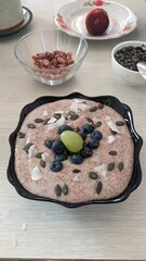 A bowl of porridge with blueberries, pumpkin seeds, and a grape