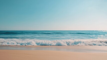 Obraz premium A serene beach scene with gentle waves lapping against golden sand under a clear blue sky. Ideal for relaxation and tranquility.