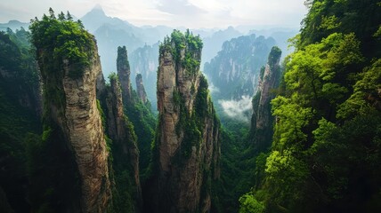 Fototapeta premium Majestic mountain pillars rise above a lush green landscape, enveloped in mist and tranquility, showcasing nature's breathtaking beauty.