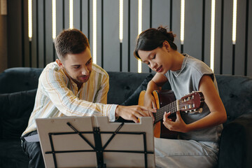 Professional instructor guiding student in playing guitar during music lesson in cozy room. Music...
