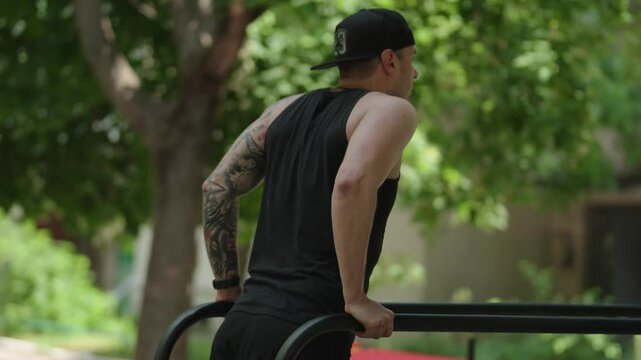 A young athletic man exercising outdoors doing dips on parallel bars. He is focused and working out hard.