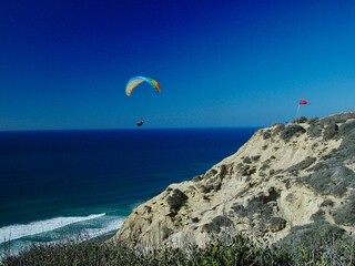 Paraglider soaring over Torrey Pines cliffs with the ocean below in California.