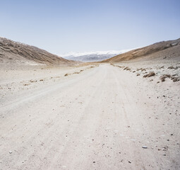 Dusty road of the Pamir Highway winds and twists in the valley of the Tien Shan Mountains against the backdrop of a mountain range with snow in Tajikistan in the Pamirs, landscape for the background