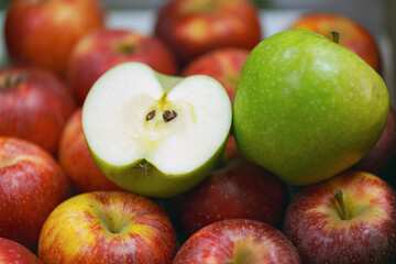 Fresh apples with a cut green apple showcasing its interior among a variety of red apples. Shiny red apples and a halved green apple. The green apple reveals its juicy white flesh and seeds. No people
