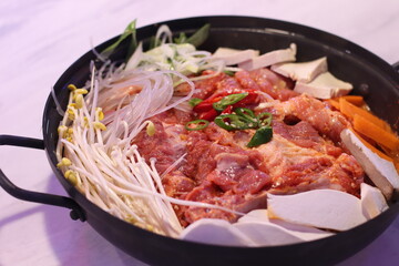 A vibrant, uncooked Korean hot pot filled with an assortment of fresh vegetables, tofu, and meat, waiting to simmer into a flavorful and hearty stew.