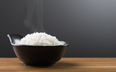 Cooked Thai jasmine rice served in a black bowl sits on a brown table against a dark grey backdrop. The studio shot highlights the fluffy texture and aromatic quality of the rice