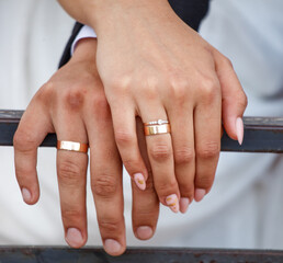 Hands of a man and a woman with golden rings on a metal fence. Close-up