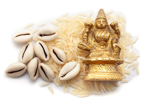 Top view of Cowries (Cypraea chinensis) placed on a pile of rice with a brass idol of the Hindu goddess Lakshmi, isolated on a white background.
