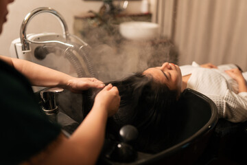 Asian woman customer get service hair care with procedure of steaming water steam and feeling relax while hairdresser massaging head at beauty salon.