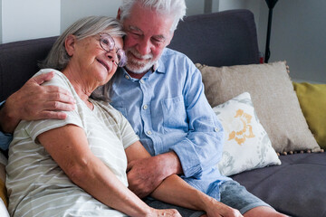 Elderly couple sitting together on a sofa at home, where the husband provides emotional support and comfort to his wife dealing with mental health issues. Highlights mature, independent living care