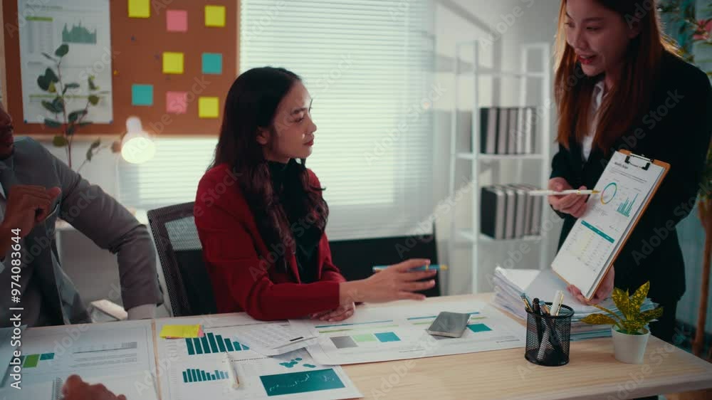 Poster two asian businesswomen are having a conversation about a financial report. one of them is holding a