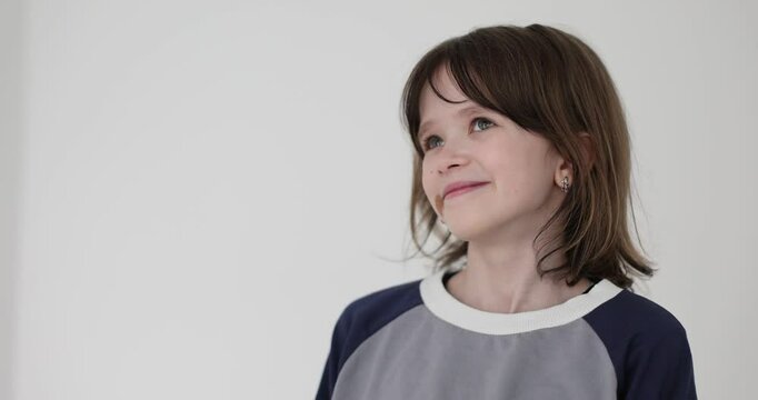 Teenage girl presses lips together and tries to suppress wave of embarrassment on white background. Kid with birthmark raises head and avoids eye contact