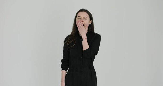 Knackered woman yawns loudly and covers mouth with hand on white background. Young female demonstrates signs of exhaustion slow motion