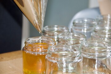 A detailed shot of honey being filled into a glass jar using a stainless steel funnel, showing the honey’s golden hue and the bottling process.