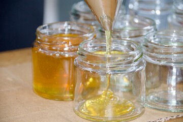 A detailed shot of honey being filled into a glass jar using a stainless steel funnel, showing the honey’s golden hue and the bottling process.