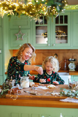 little daughter with mother make dough for traditional Christmas cookies, cooking together in cozy kitchen during winter holidays