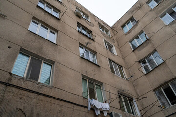 A dilapidated Soviet-era apartment building in Bishkek, Kyrgyzstan, showing signs of wear and tear with crumbling concrete and faded windows. The structure's aged appearance is a stark reminder of the