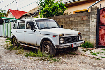 A vintage white Soviet-era Lada parked on a quiet, tree-lined residential street in Bishkek,...