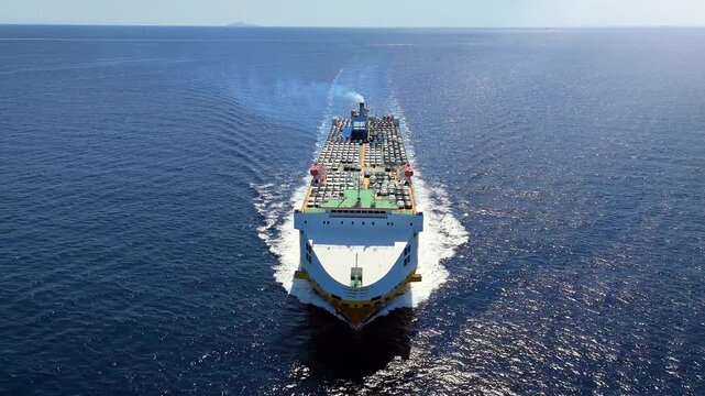 Aerial front view of a large, industrial car carrier transport ship cruising with speed over the ocean