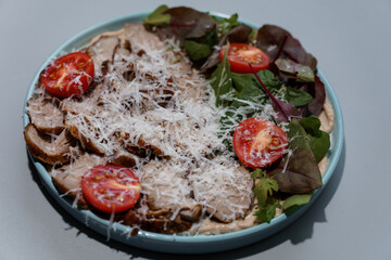 Delicious Sliced Pork with Fresh Greens and Cherry Tomatoes Garnished with Grated Cheese on Blue Plate