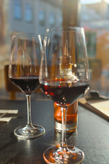 Two wine glasses with red wine and a bottle with chili oil on a table in a restaurant in backlight with reflections