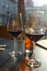 Two wine glasses with red wine and a bottle with chili oil on a table in a restaurant in backlight with reflections