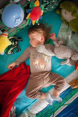A peaceful toddler sleeping soundly in a colorful play area surrounded by soft toys and cozy blankets
