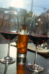 Two wine glasses with red wine and a bottle with chili oil on a table in a restaurant in backlight with reflections
